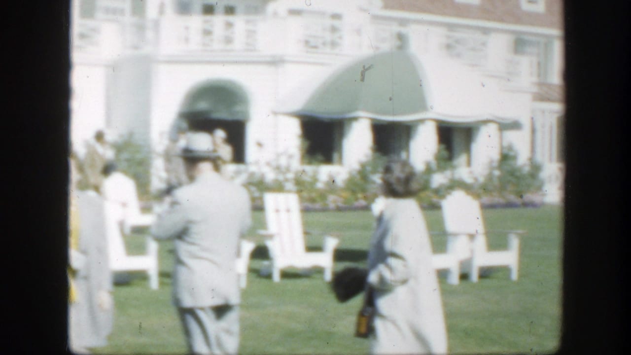 People on a lawn near white chairs and a white building, partly obscured by film frame divisions.