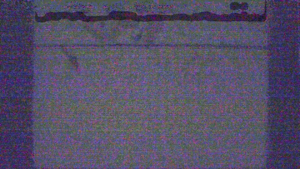 A heavily degraded 8mm frame shows faint architectural detail and strong grain, with the scene mostly obscured.