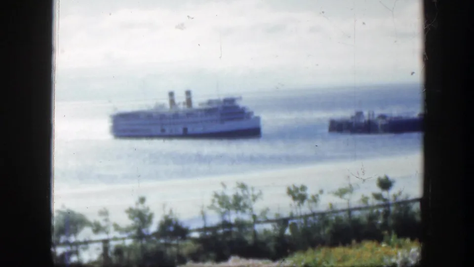 A soft 1950 Montreal waterfront view shows the ship farther across the water, with flowers, shrubs, railing, and dark frame edges in front.