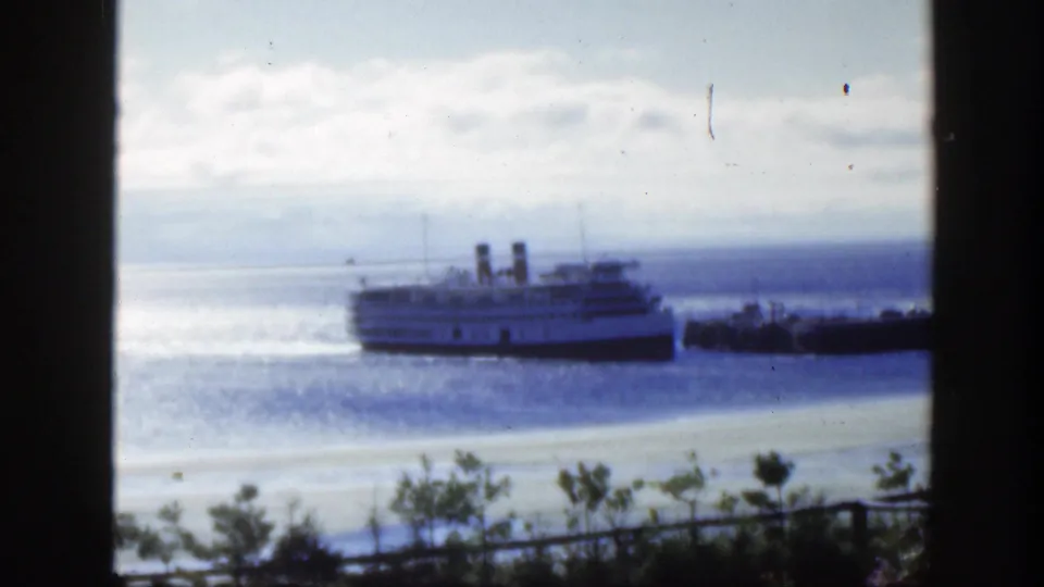 A soft 8mm frame from 1950 Montreal shows a passenger ship near a pier, with water, pale sky, shoreline brush, and dark window framing.
