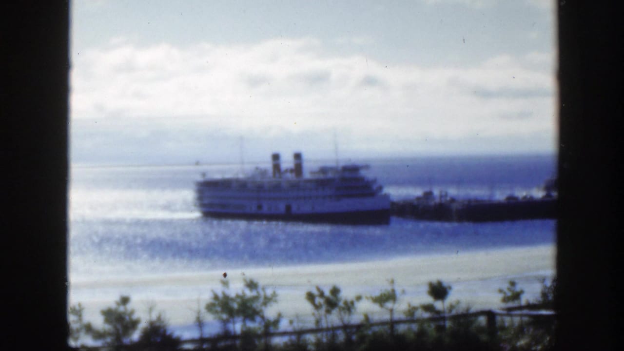 1950 Montreal-area 8mm frame showing a twin-stack passenger ship on water beyond a shoreline, viewed through dark vertical window framing.