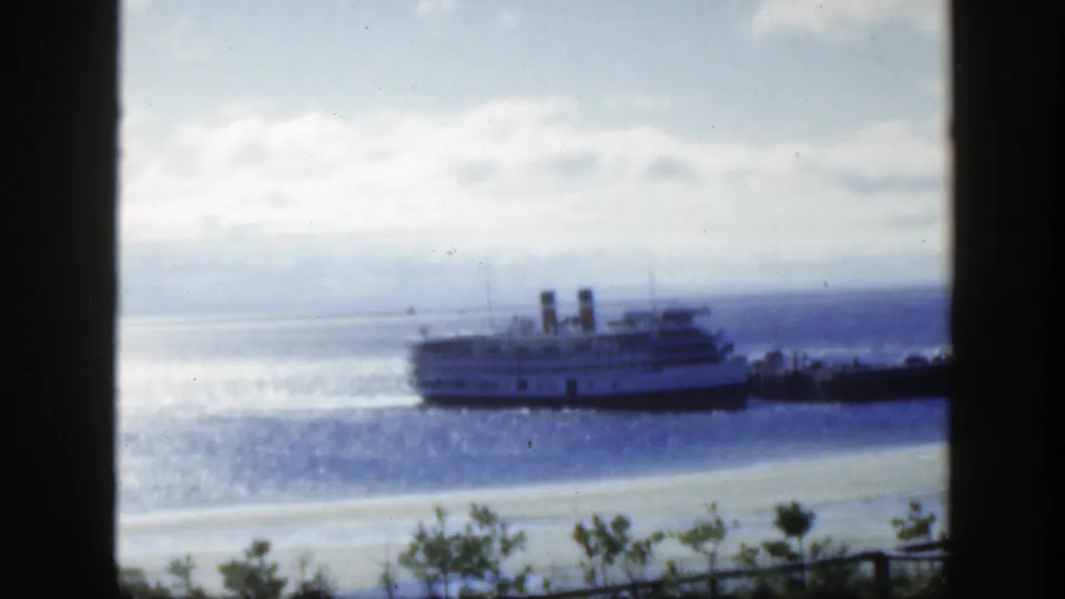 1950 Montreal-area home-movie frame with a passenger vessel moving across bright water under a cloudy sky, partially bordered by dark framing.