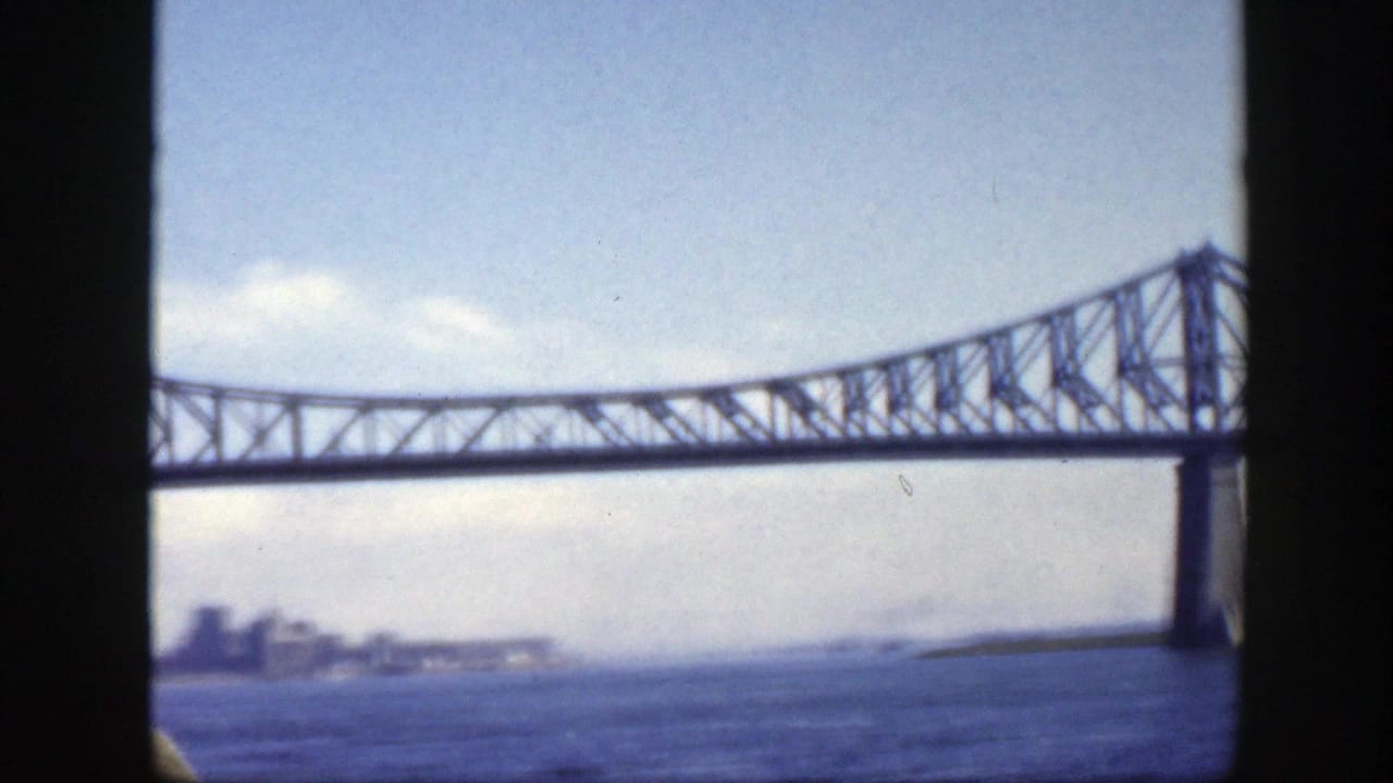 1950 Montreal home-movie frame showing the Jacques-Cartier Bridge crossing water, with a distant shoreline and skyline at left.