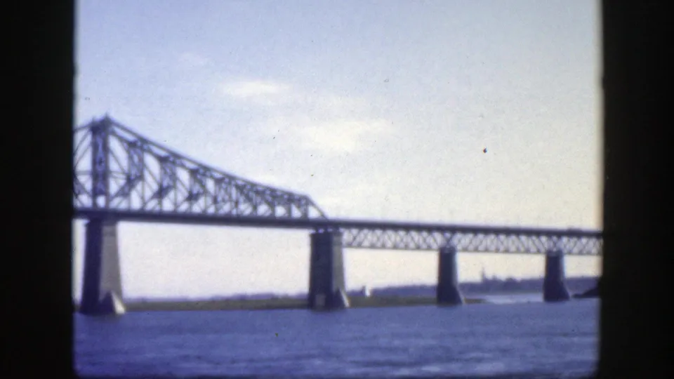 Final 1950 Montreal frame showing the Jacques-Cartier Bridge stretching across the river, with piers and skyline in the distance.