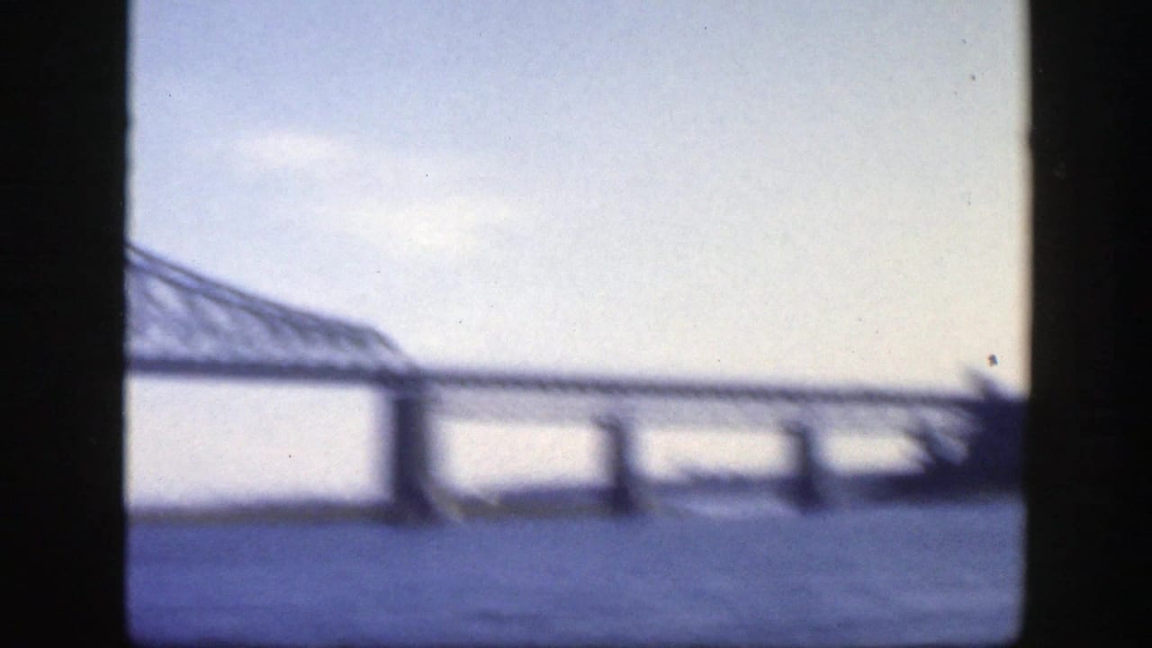 1950 Montreal 8mm frame showing a long steel truss bridge over a wide river, partly soft and bordered by dark film edges.