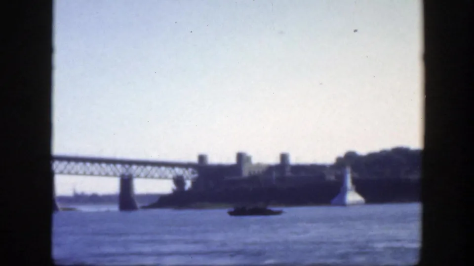 1950 Montreal 8mm frame showing a small boat on the river, bridge span at left, distant buildings, and a white lighthouse-like structure.