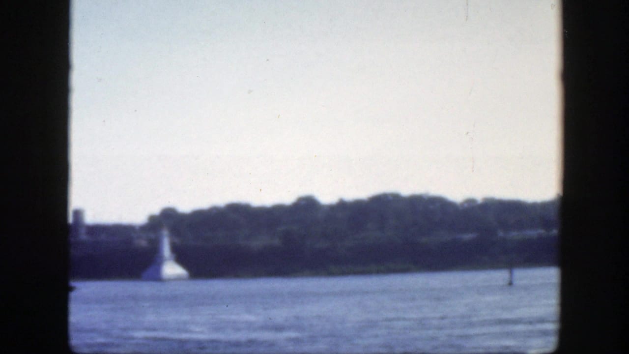 A soft 1950 Montreal riverfront view shows water, a distant wooded bank, a white conical shoreline structure, and a small channel marker.