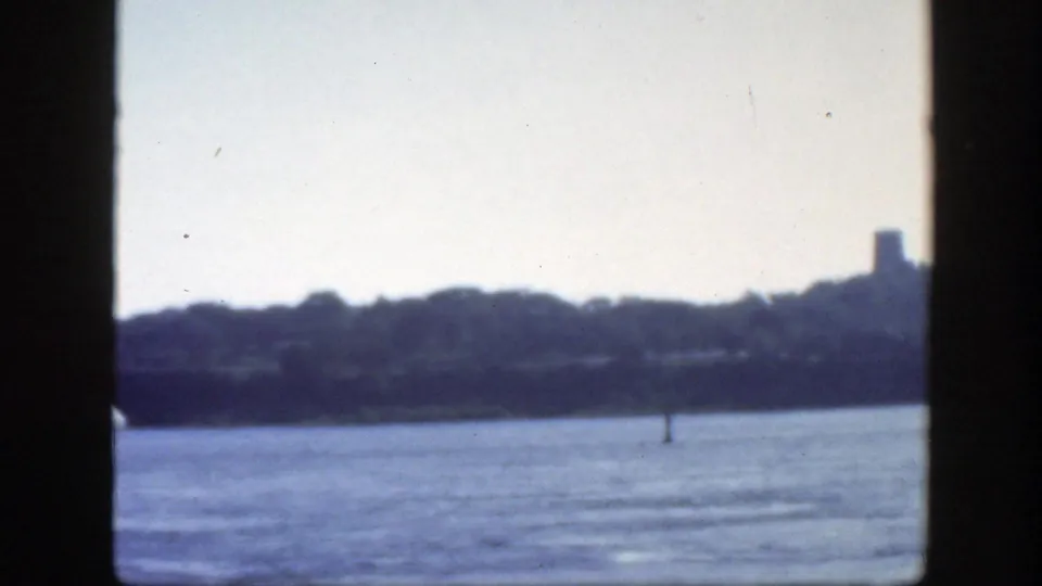 1950 Montreal footage frames a hazy river and wooded shoreline, with a distant tower shape and small marker visible near the water.