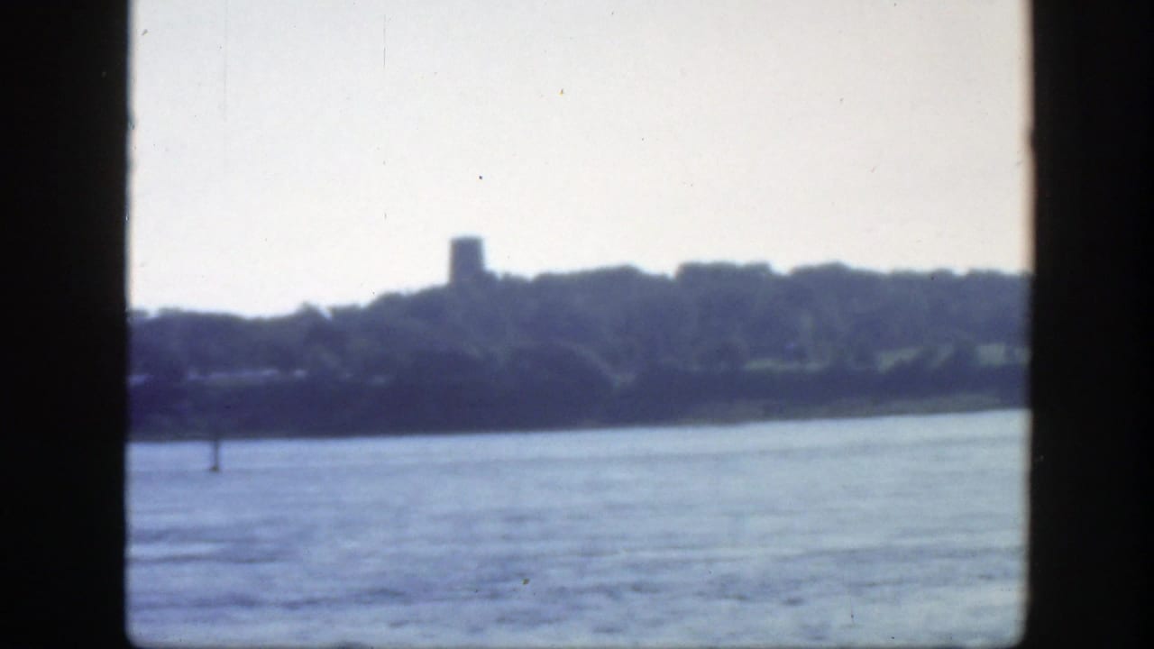 1950 Montreal-area 8mm view across bright water toward trees and a small tower-like form on the far shore.