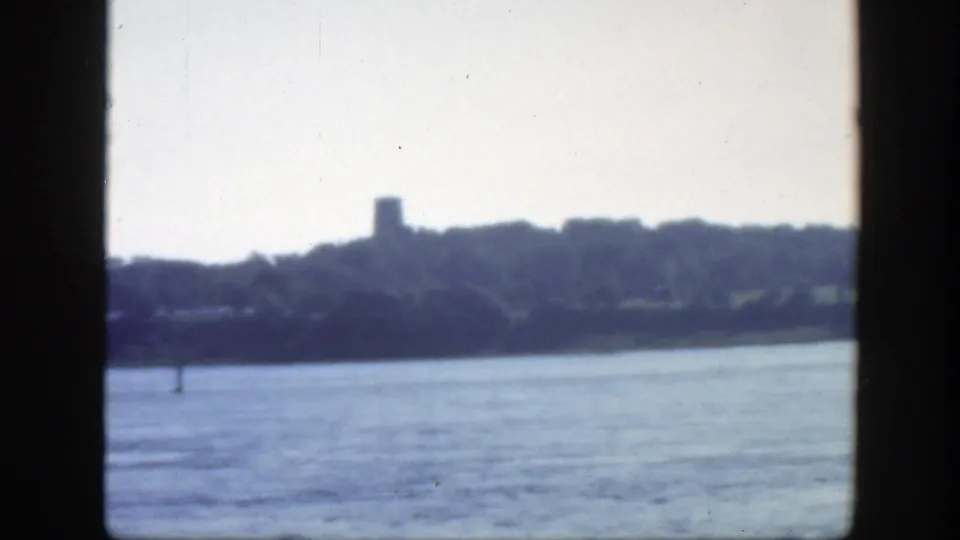 1950 Montreal-area 8mm view across bright water toward trees and a small tower-like form on the far shore.