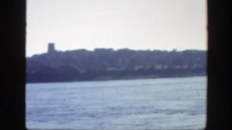 1950 Montreal-area 8mm frame with soft-focus water in the foreground and a hazy wooded shoreline beyond.