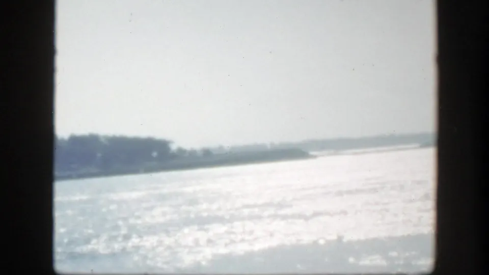 1950 Montreal-area 8mm frame showing sunlit water and a low, tree-lined shore fading into a hazy distance.