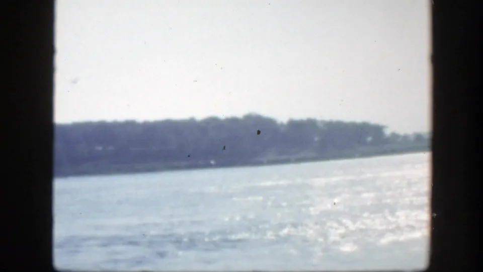 1950 Montreal waterfront view with bright glare on the water and a wooded shoreline beyond dark frame bars.