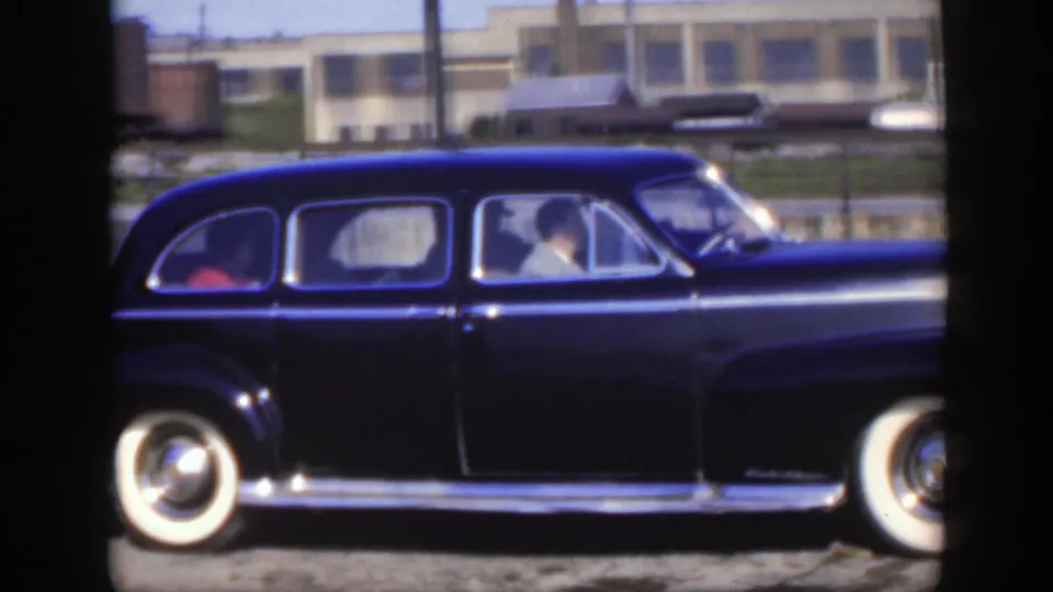 1950 Montreal frame showing the black sedan side-on with whitewall tires and rail-yard structures in the background.