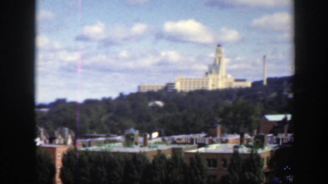 Distant pale building on a wooded hill above city rooftops under a cloudy sky.