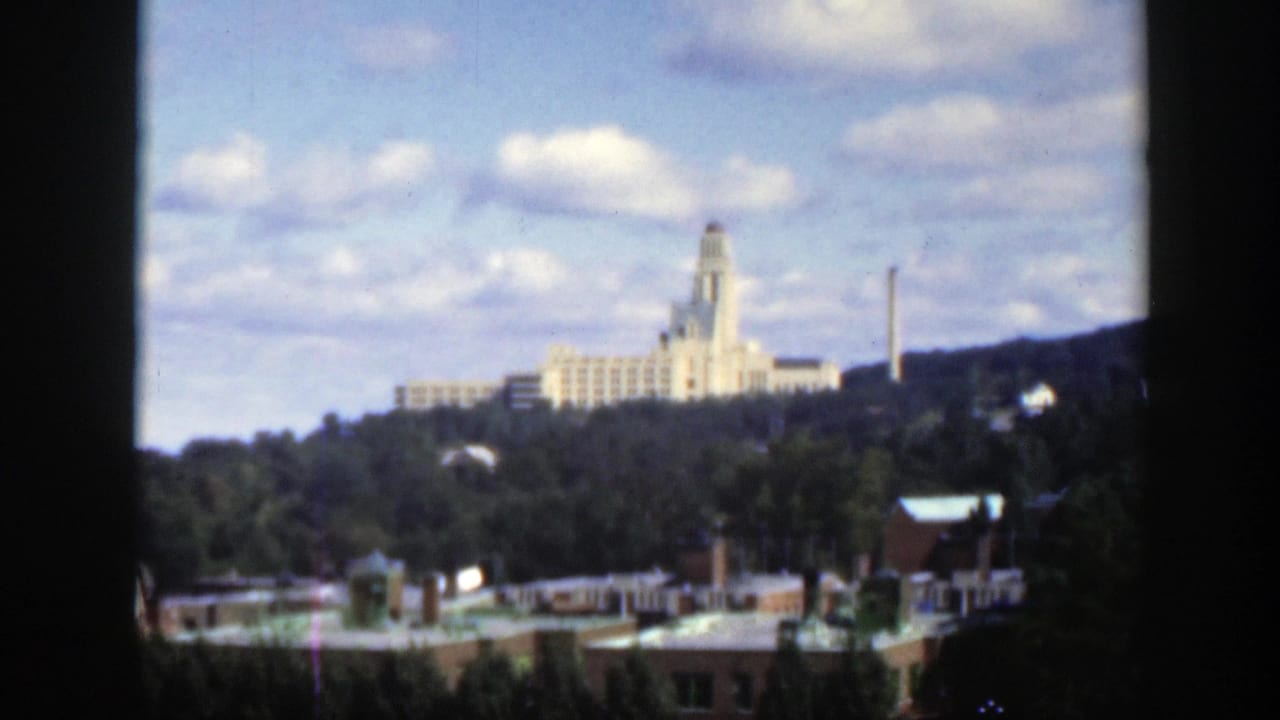Wide city view with a large pale building on a hill and rooftops in the foreground.