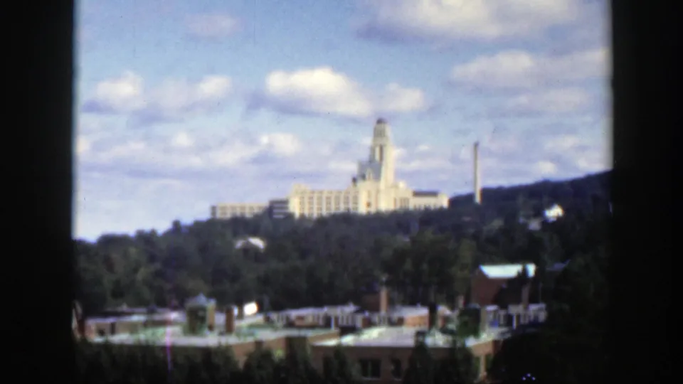 1950 Montreal view across rooftops and trees toward a large pale building on a hill, framed by 8mm film borders.