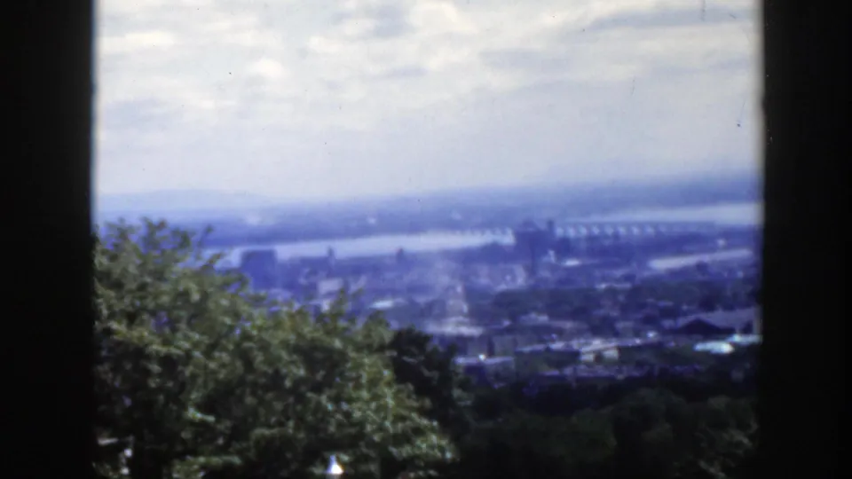 1950 Montreal home-movie view looking across trees toward a hazy cityscape, river, and distant bridge.