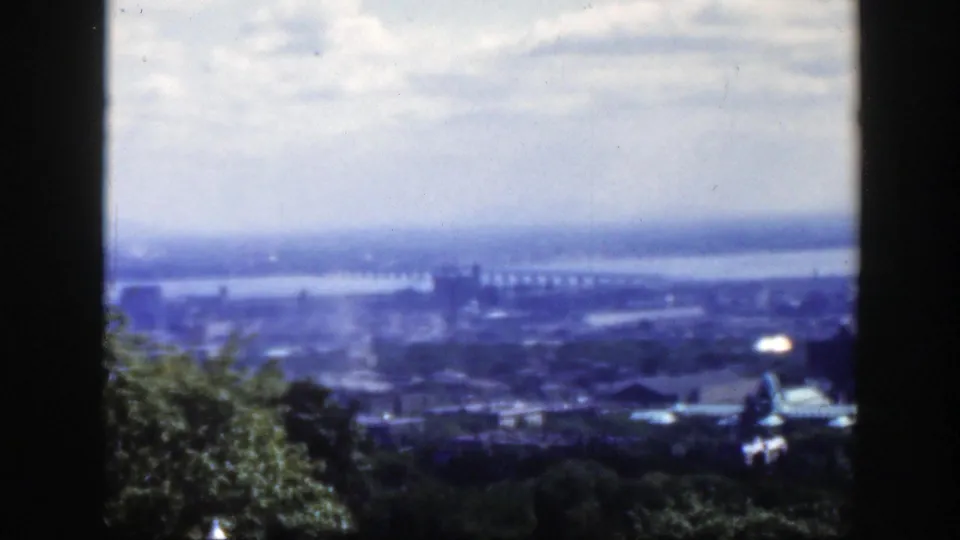 1950 Montreal frame showing a broad elevated city view with river, bridge, treetops, and a small dome at the lower right.