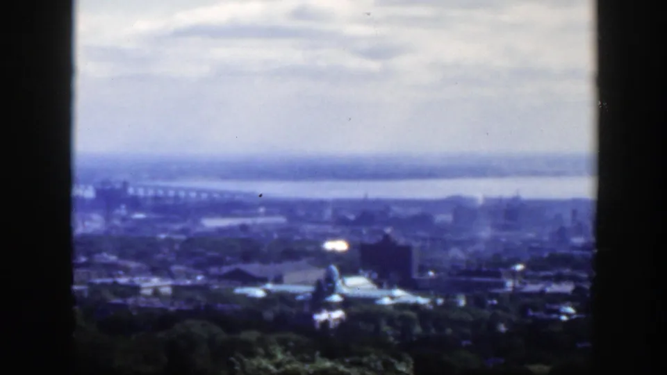 1950 Montreal skyline panorama in soft focus, with a wide waterway, distant bridge, domed building, cloudy sky, and dark frame edges from an elevated viewpoint.
