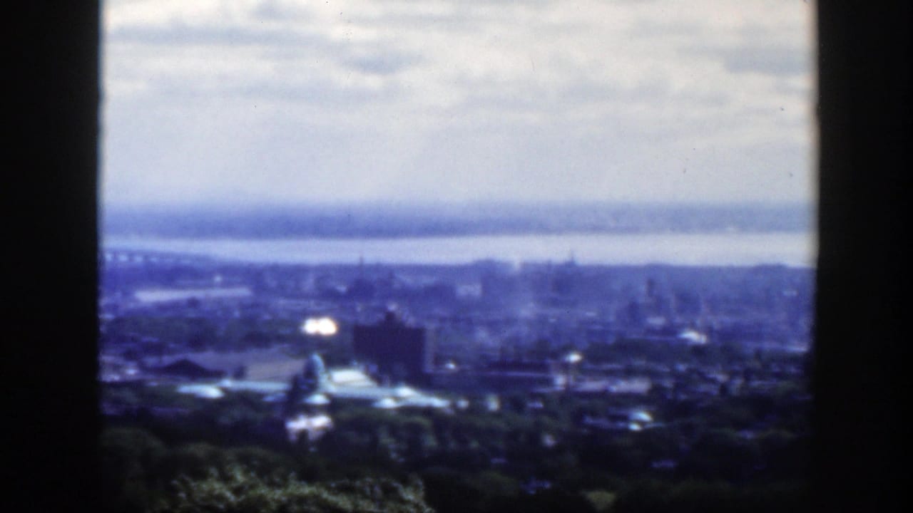Blue-tinted skyline view with water beyond the city and a bright reflection near a dome.