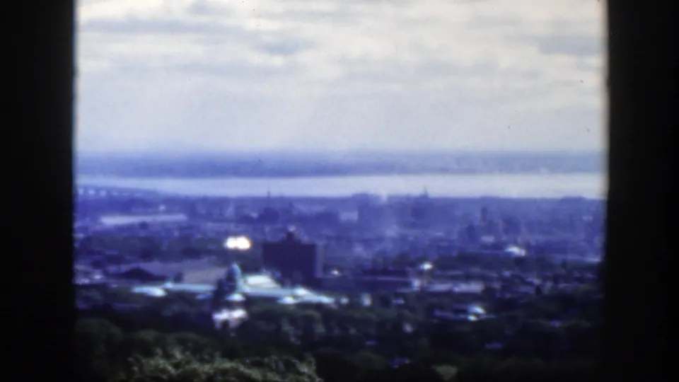 Blue-tinted 1950 Montreal view from above, showing dense buildings, a broad waterway, bridge line, prominent dome, cloudy sky, and dark side framing.