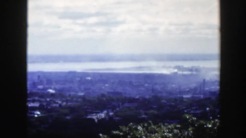 Late frame of the 1950 Montreal panorama, showing foreground trees, blue-toned buildings, distant river, haze, and dark window borders.