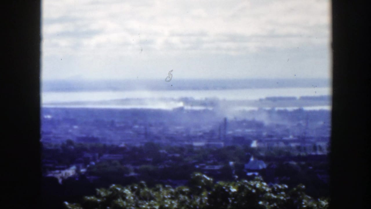 Hazy Montreal cityscape seen from above on 8mm film, with distant water and industrial-looking smoke or mist.