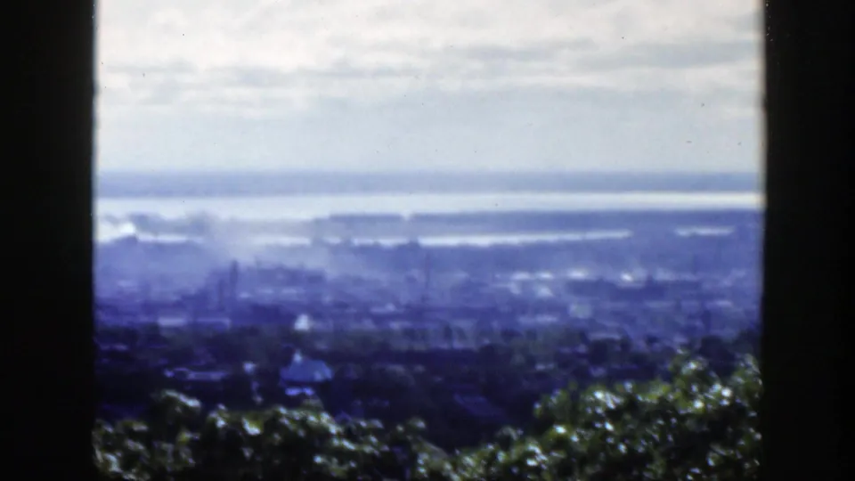 Montreal appears in a blue-tinted 8mm frame, with foreground treetops, distant city structures, haze, and water beyond.