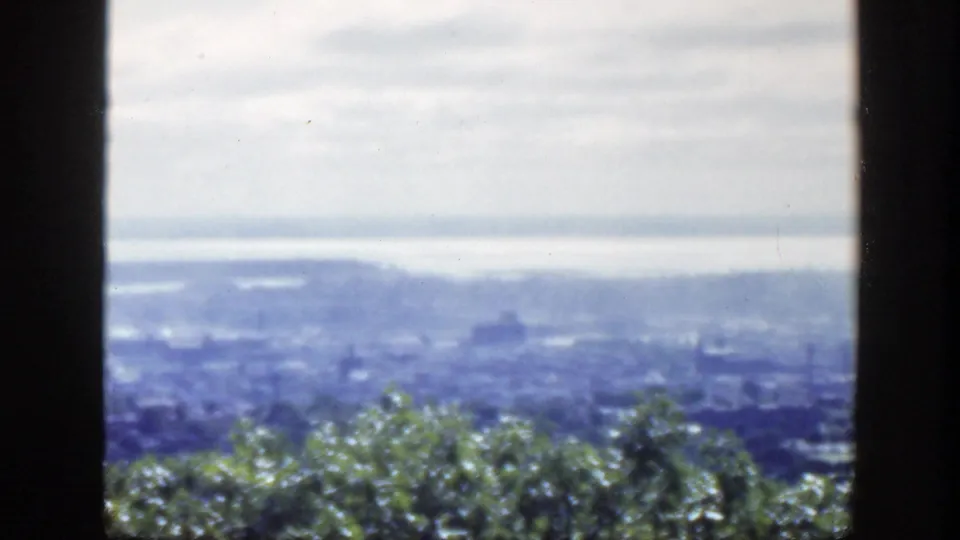 Hazy 1950 Montreal overlook with green trees in front and a wide water body beyond the city.