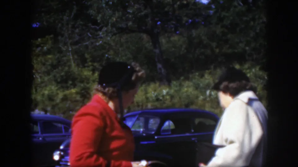 Two women in period attire stand beside a dark car at a wooded Montreal overlook in 1950 home-movie footage.