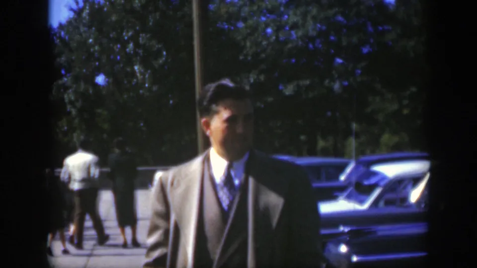 The man in a suit turns slightly in the Montreal parking area as pedestrians and classic cars remain visible in the background.