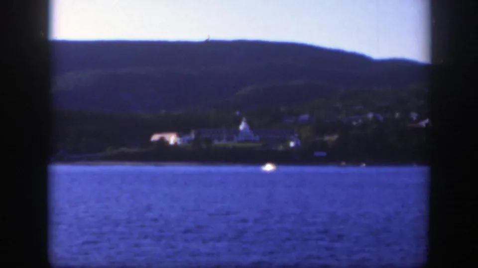1950 8mm view across a lake near Montreal, with distant buildings at the waterline and dark hills behind them.
