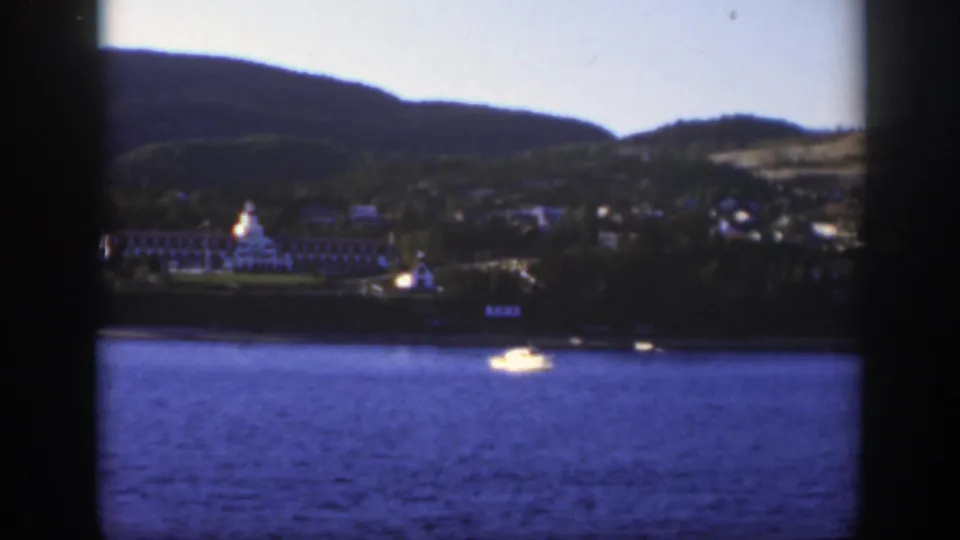 1950 8mm lakeside view near Montreal with the resort building more centered, a small boat on the water, and wooded hills beyond.