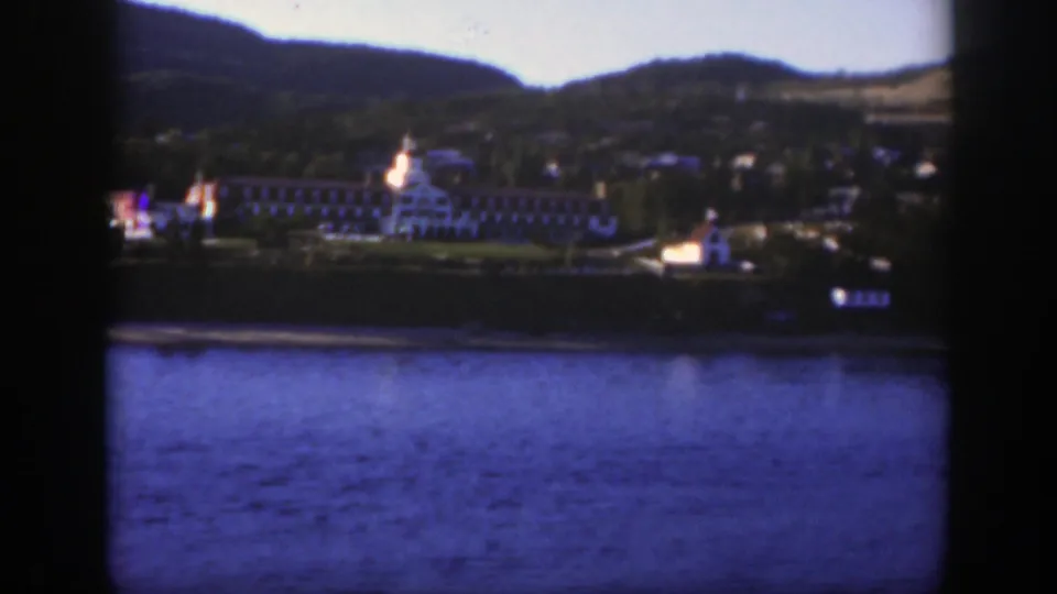 A distant resort complex along a calm lake near Montreal, with a prominent white building, shoreline structures, and hills in the background.
