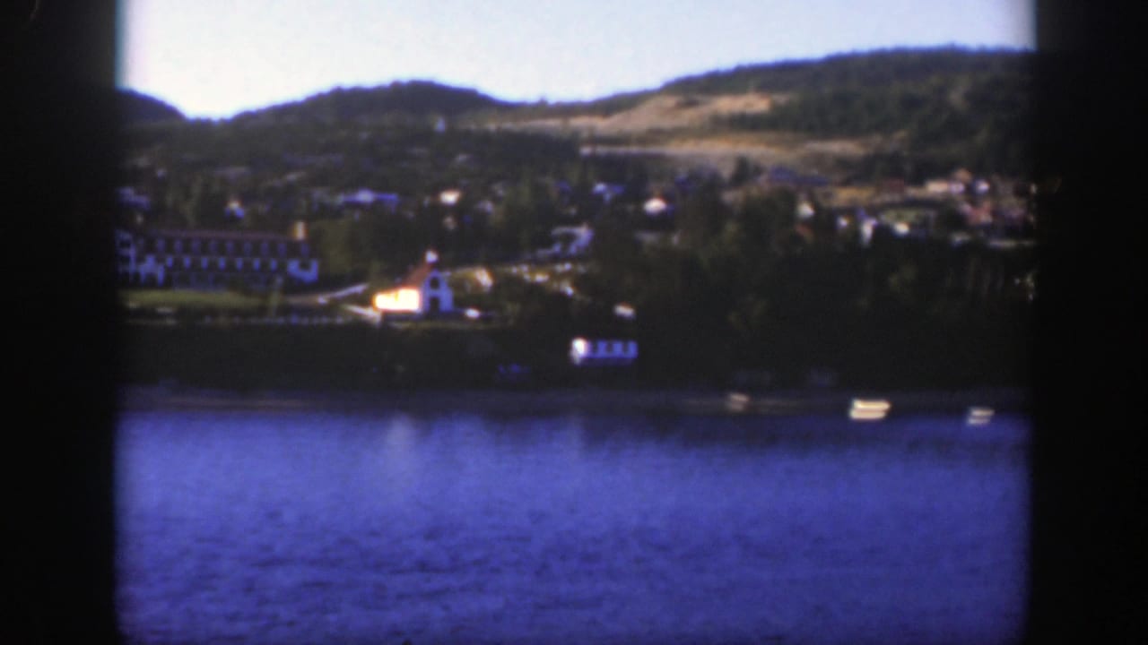 Blue lake with distant shoreline buildings and green hills beyond.