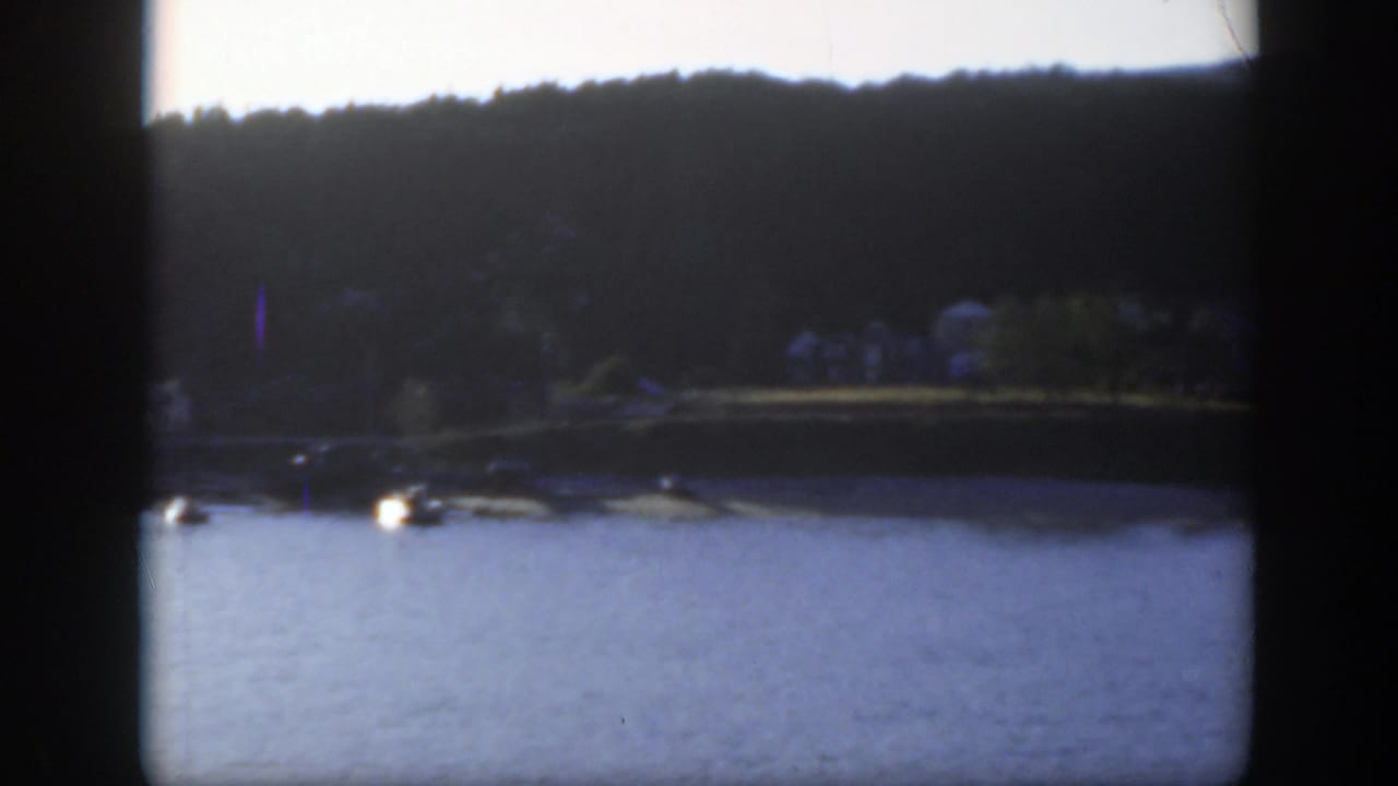 1950 Montreal home-movie frame showing water, a tree-lined shore, and small houses seen from a boat.