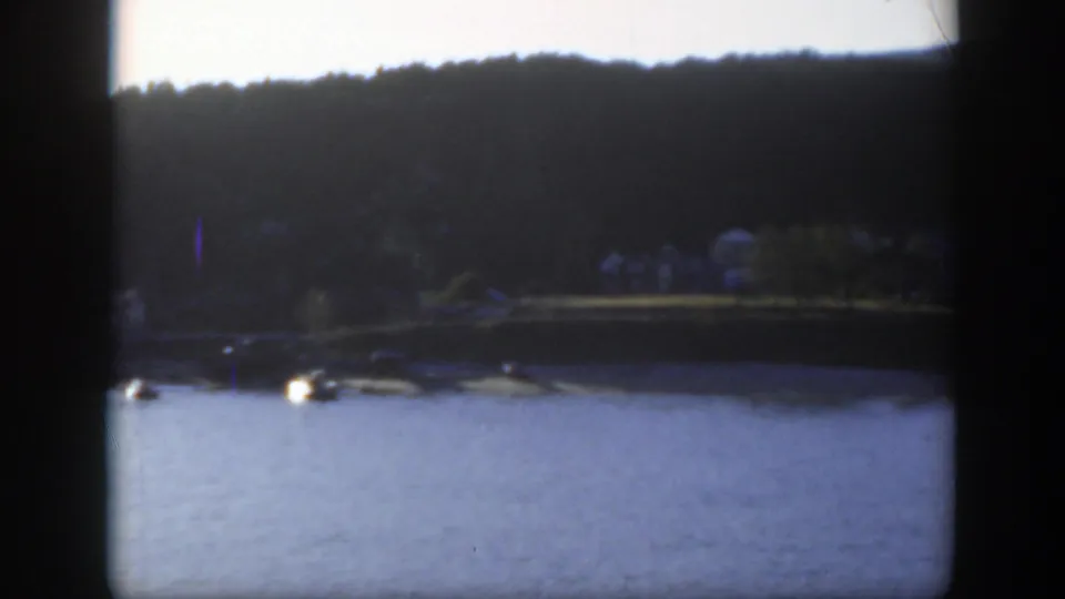 1950 Montreal home-movie frame showing water, a tree-lined shore, and small houses seen from a boat.