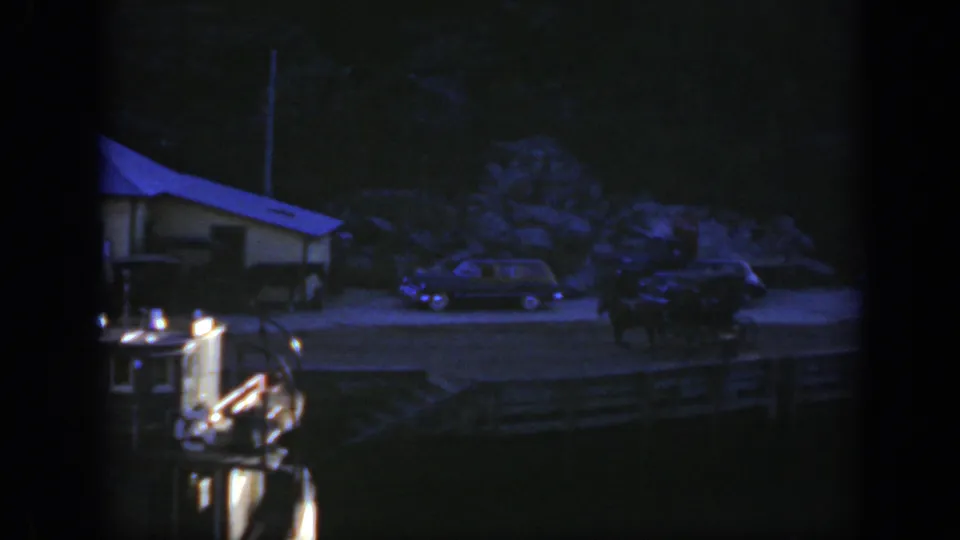 Late 1950 Montreal boat view with a small waterfront building, several parked cars, railings, and deep blue 8mm low-light color.