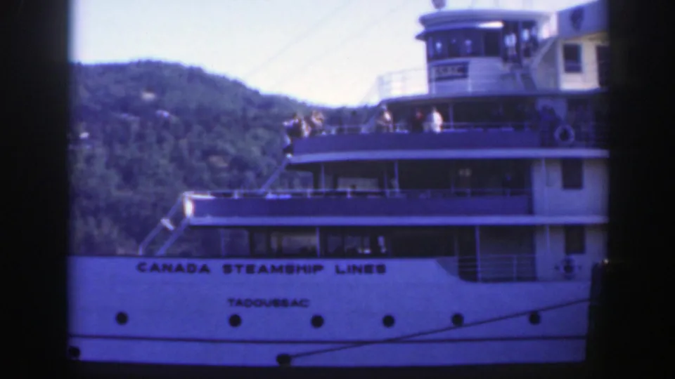 1950 Montreal home-movie frame of the Tadoussac passenger vessel with people on deck, railings, windows, and a tree-covered hill.