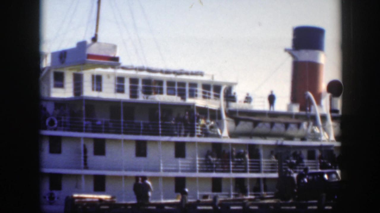 Passenger ship side with smokestack, railings, dock figures, and car at the pier.