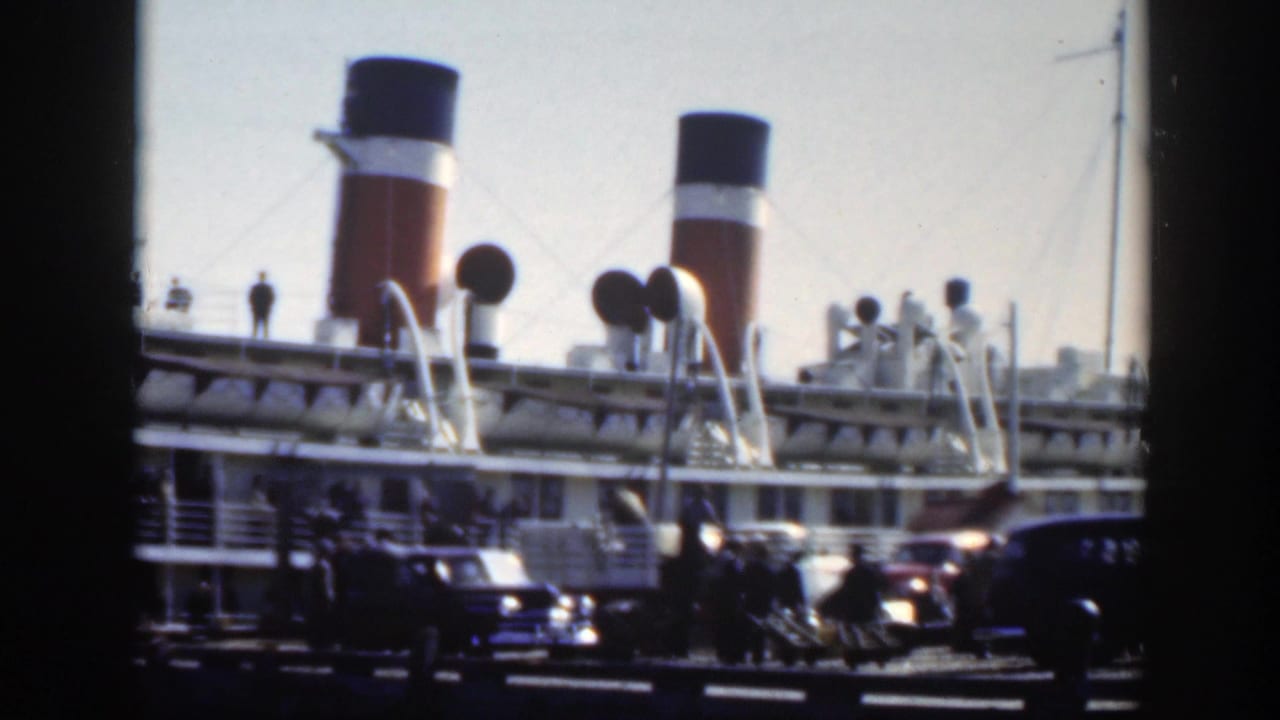 Montreal port scene showing a docked liner, prominent funnels, deck structures, parked automobiles, and small groups of people.