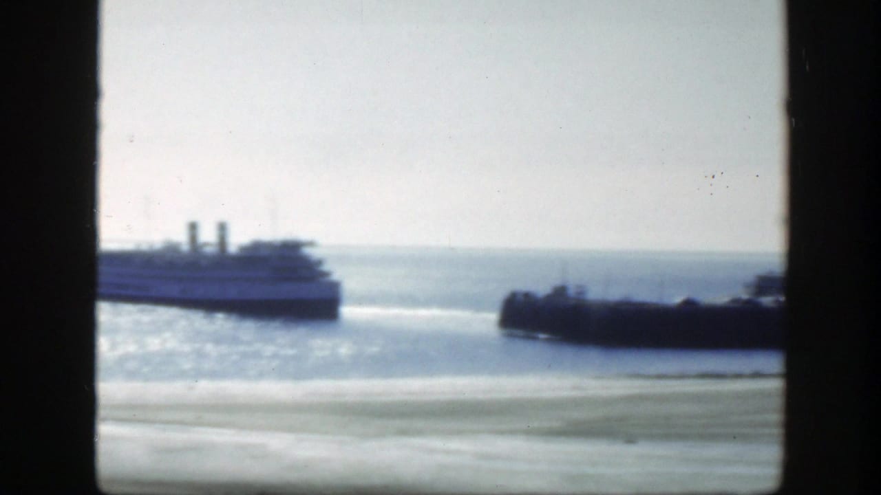 1950 8mm frame near Montreal showing a passenger ferry beside a pier or breakwater under a pale sky.