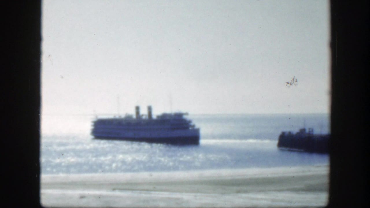 Passenger boat on sunlit water with a pier or breakwater at right.