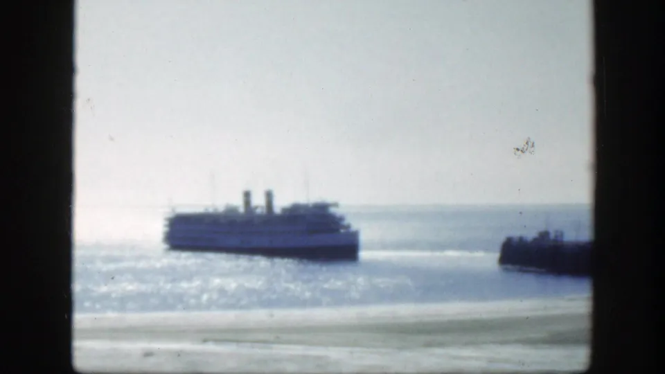 1950 8mm Montreal-area waterfront shot showing a passenger boat moving across sunlit water near a pier or breakwater.