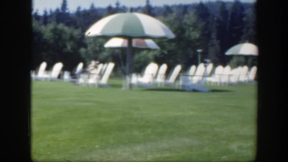 1950 Montreal resort lawn with rows of white chairs, striped shade umbrellas, and dark trees in the background.