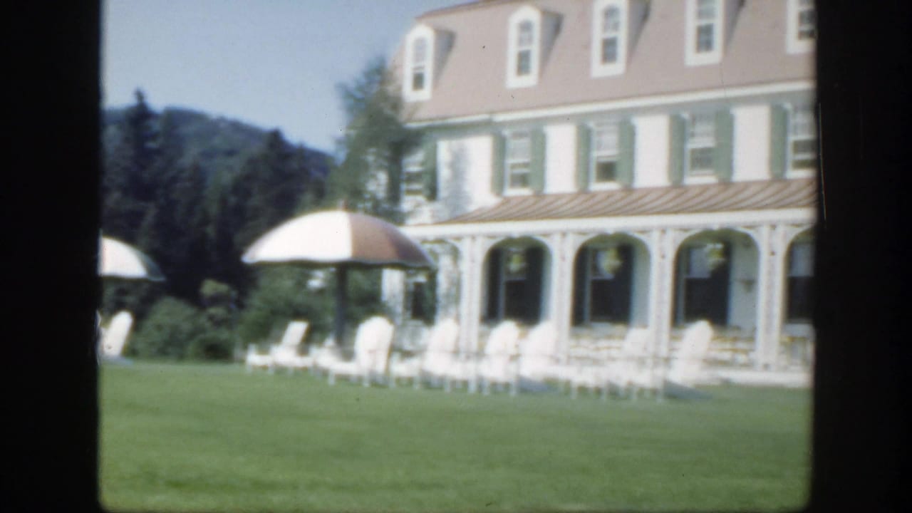 White hotel with green shutters, veranda, lawn chairs, and striped umbrellas.