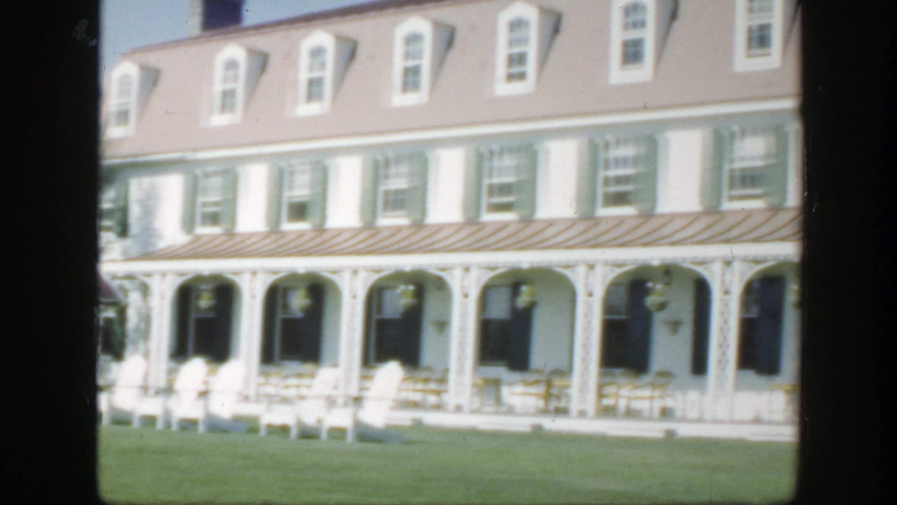 Hotel porch with repeated arches, white chairs, green shutters, and lawn.