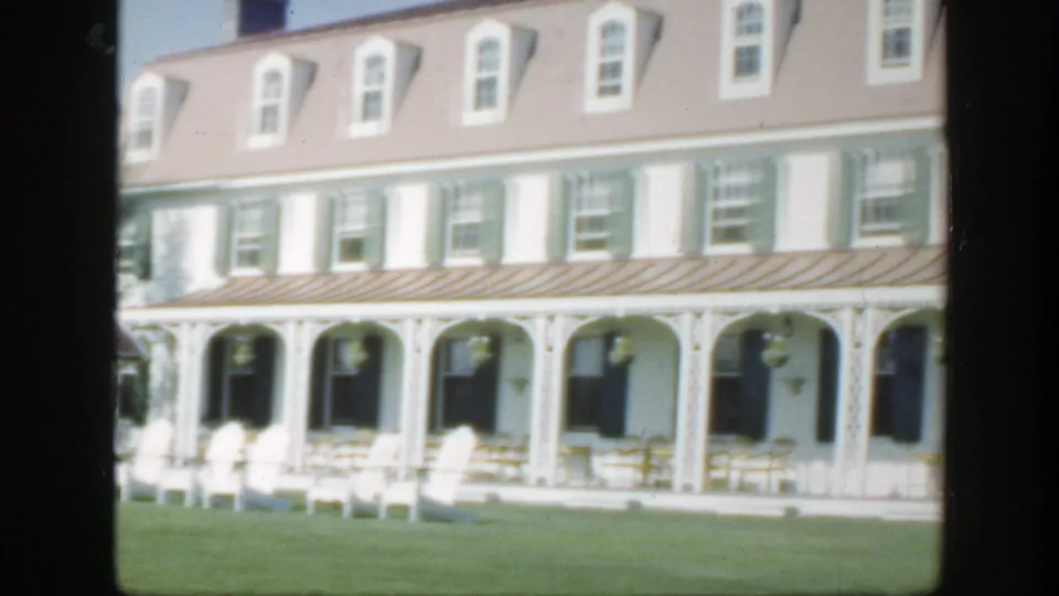 1950 Montreal home-movie view of the hotel veranda, arched porch supports, green shutters, white chairs, and open lawn.