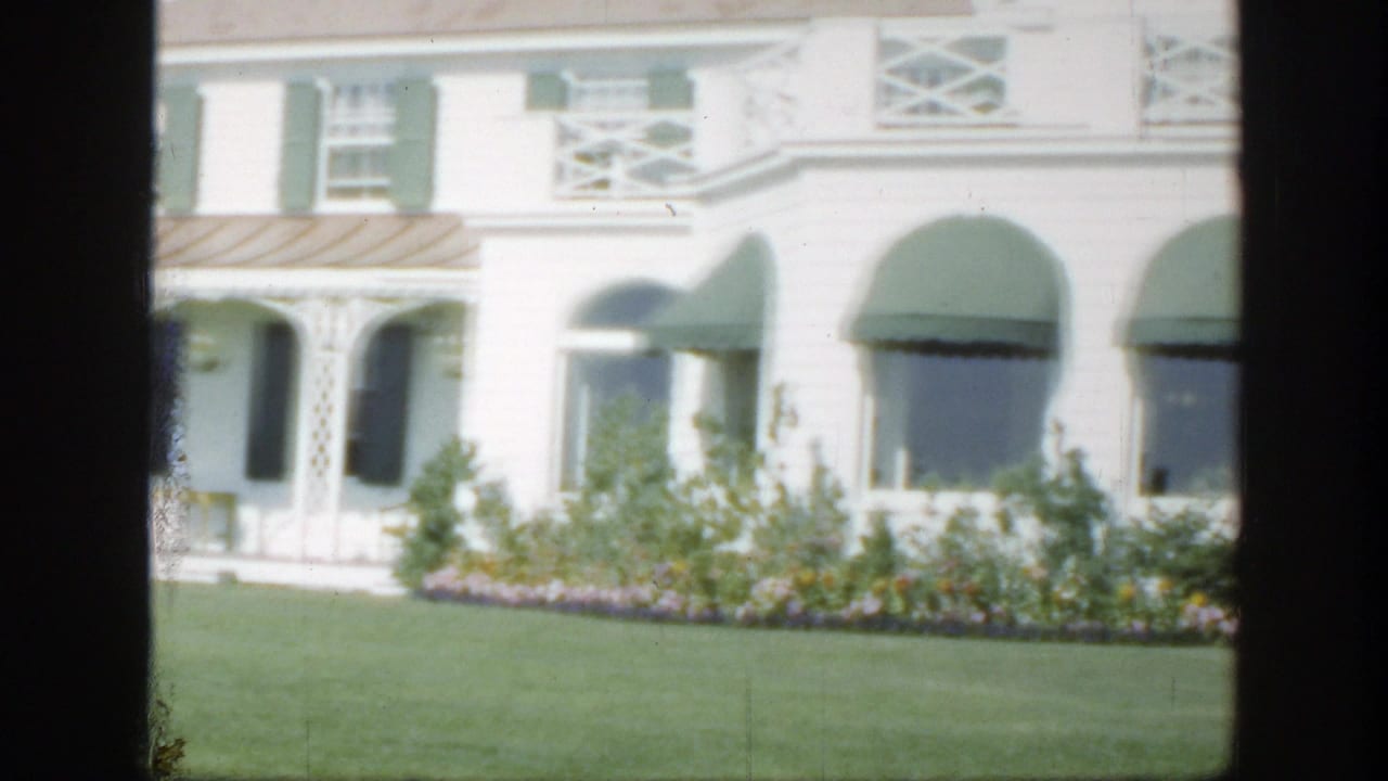 1950 Montreal 8mm view of a white building with green awnings, shutters, flower beds, and trimmed grass.